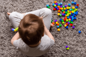 niño sentado sobre la alfombra con las piernas cruzadas juega con legos multicolores